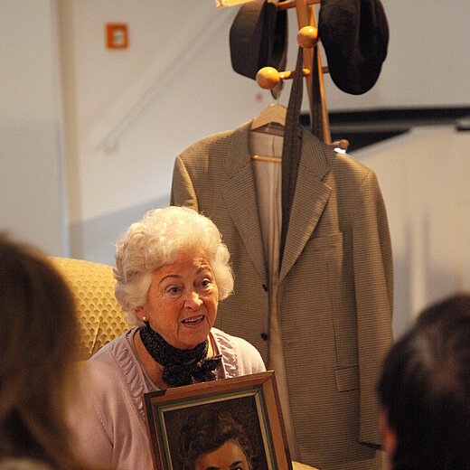 ältere Frau mit Bild in der Hand, im Hintergrund alte Möbel